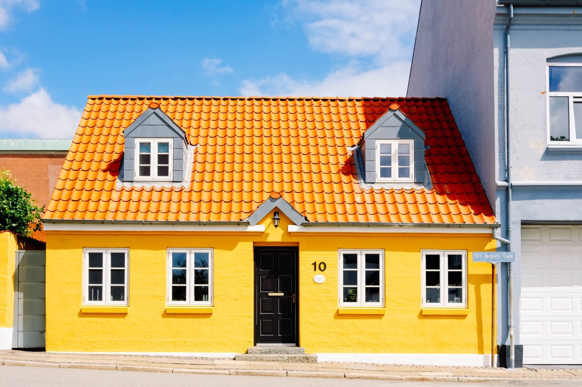 Gulputsad villa med orange tegeltak och takkupor, snygg fasadmålning som lyfter fasaden.
