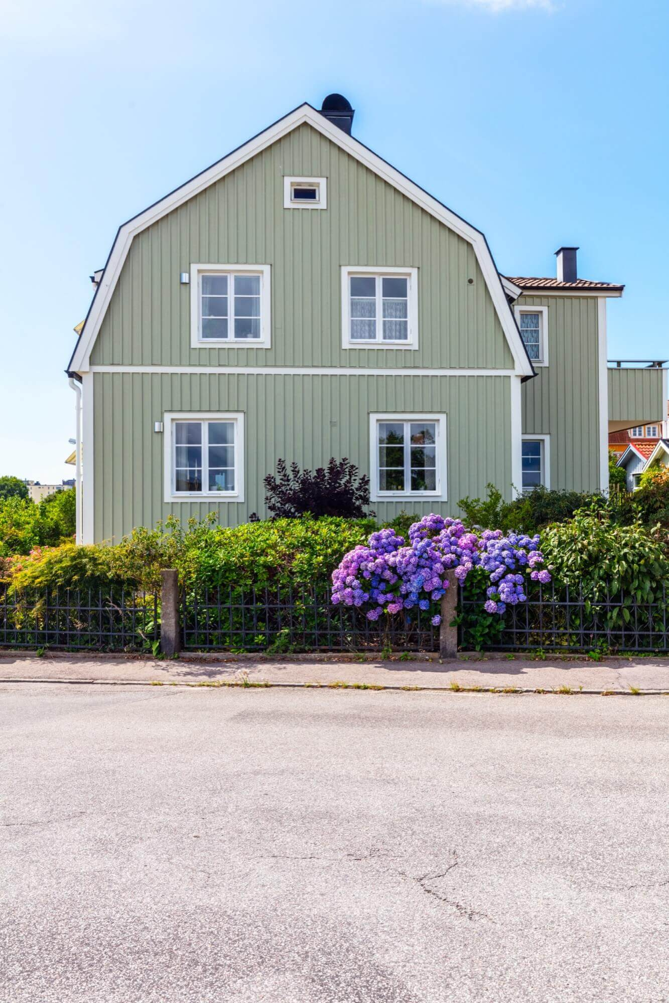 Ljusgrön trävilla med vitmålade detaljer och blommande hortensior framför, resultat av omsorgsfull fasadmålning.