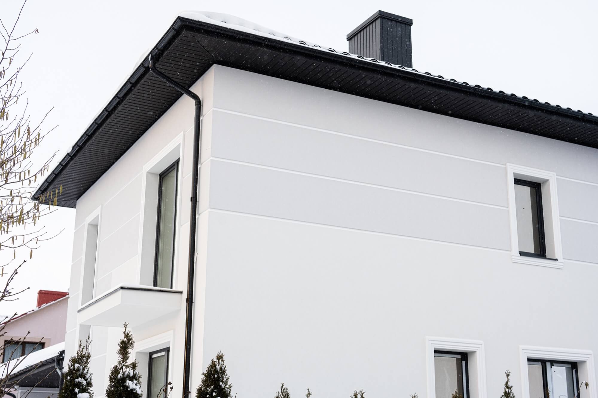 Modern tvåplansvilla med vit putsad fasad och svarta detaljer i vinterskrud, ett stilrent exempel på fasadmålning.