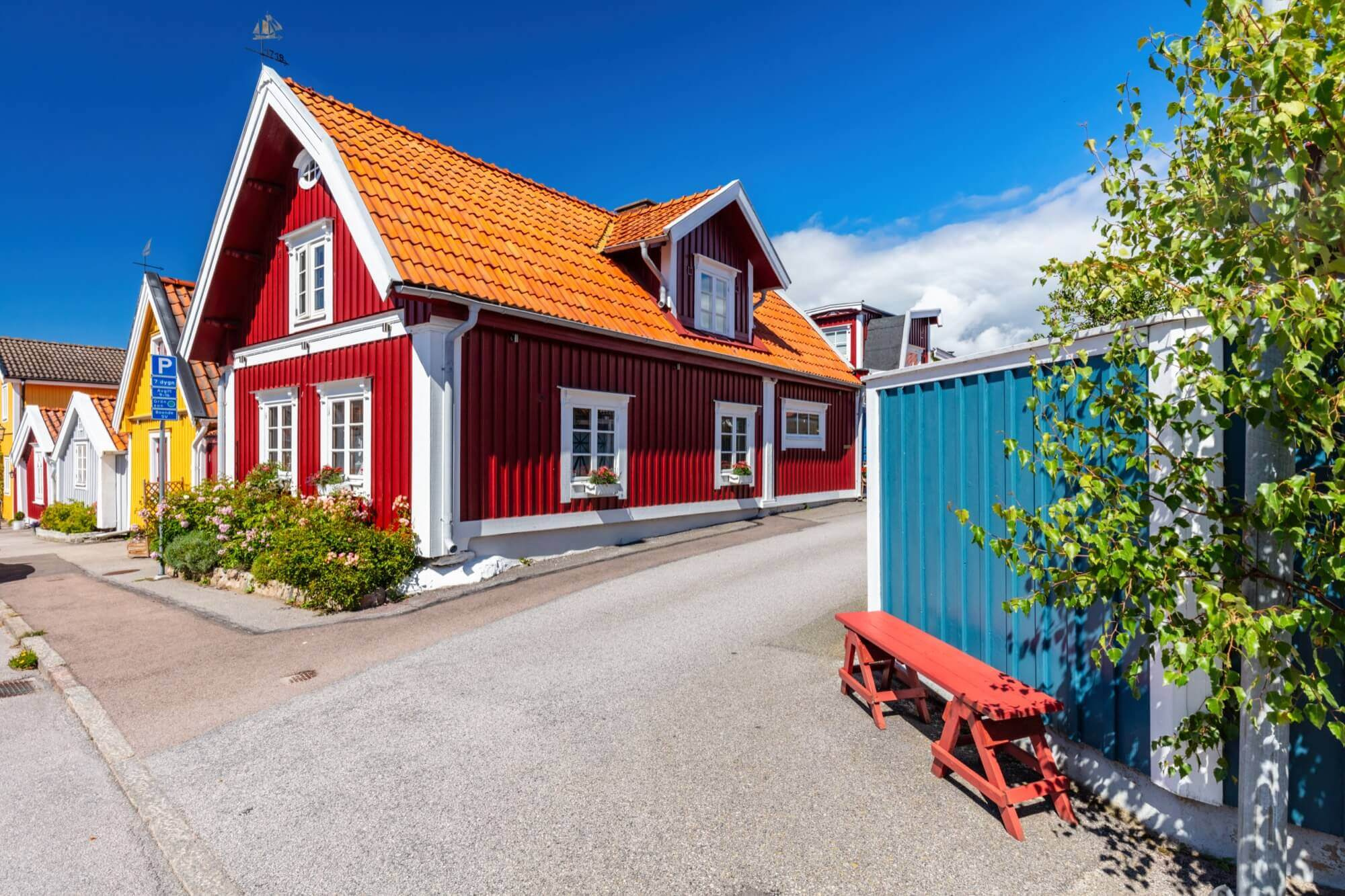 Röd träfasad med vita knutar och orange tegeltak i en kustnära by, klassisk fasadmålning i starka färger.